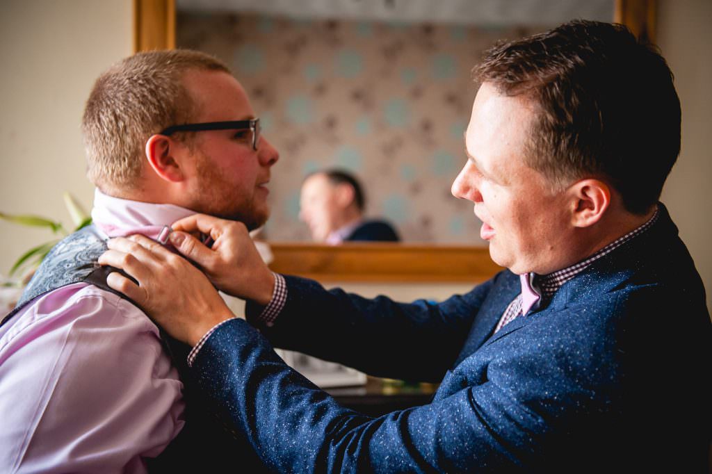 best man assists groom with bow tie