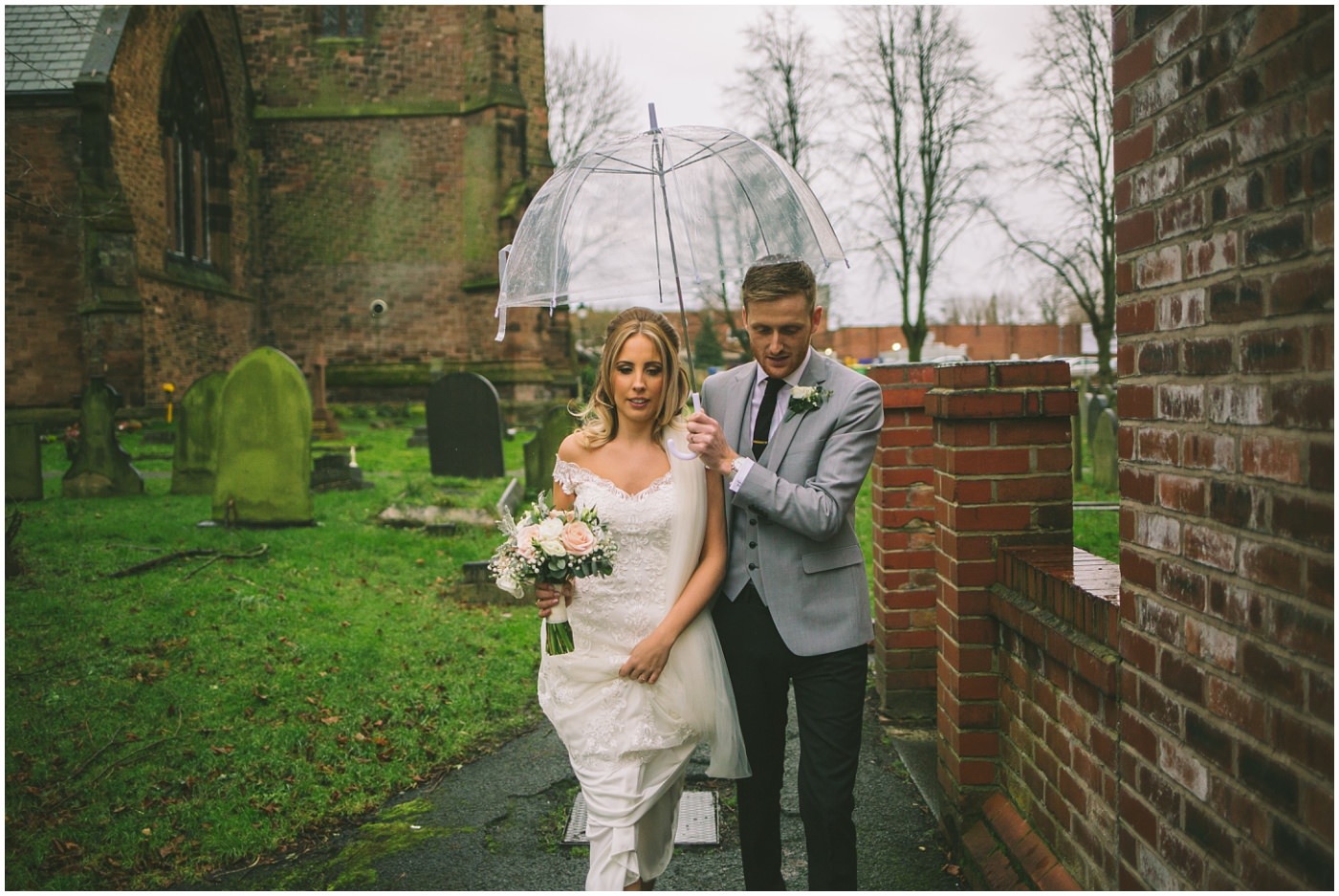 Groom holds umbrella over his bride as they exit the church 