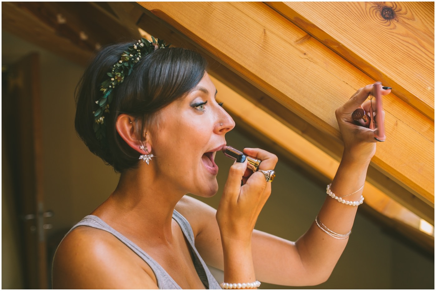 Bride applies lipstick in windowlight
