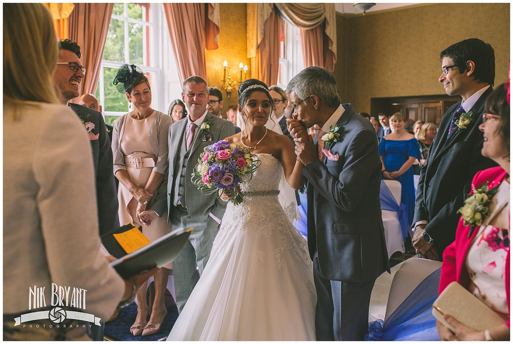 Father kisses his daughters hand as he hands her to the groom at shrigley hall wedding
