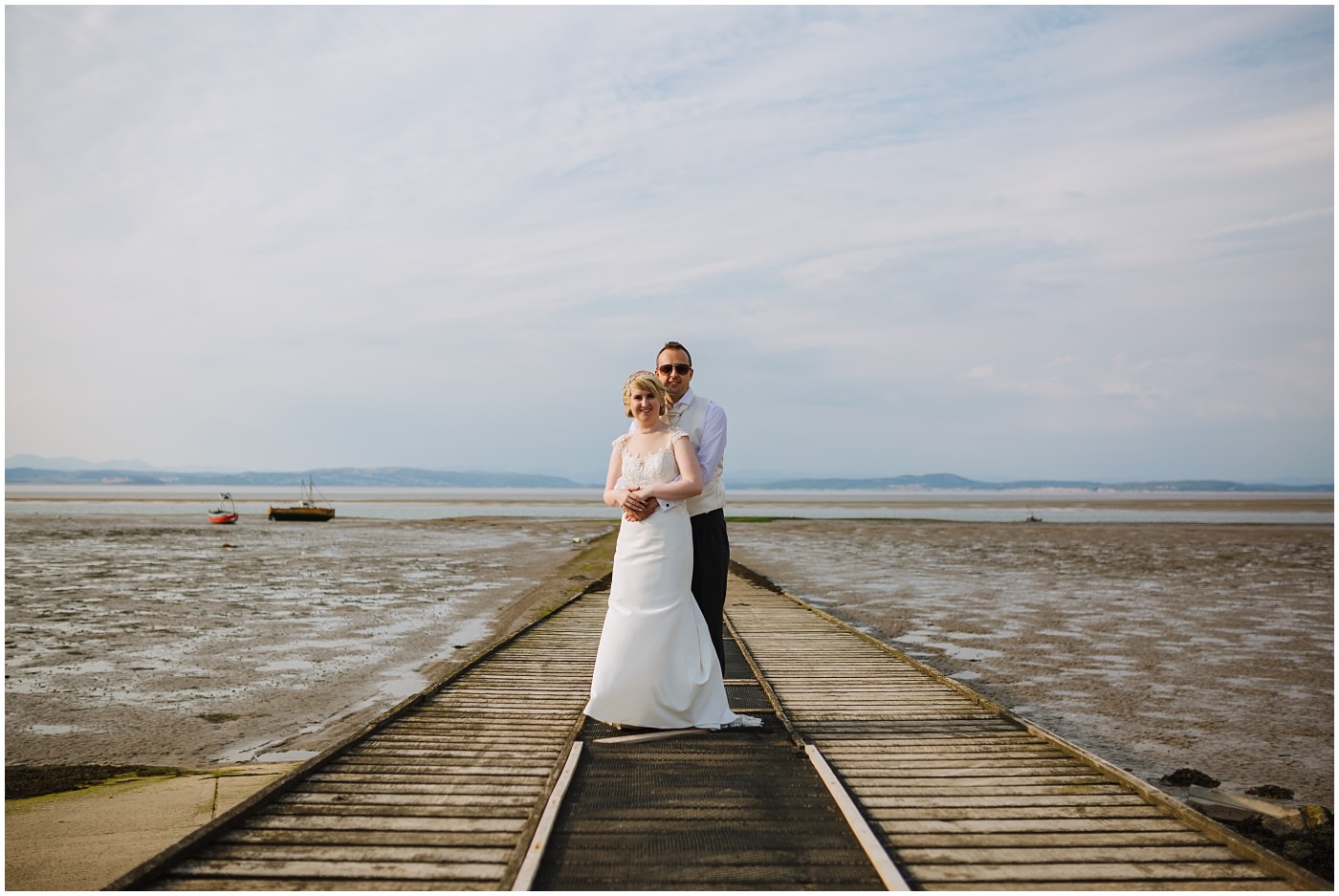 bride and groom embrace on pier at seaside wedding