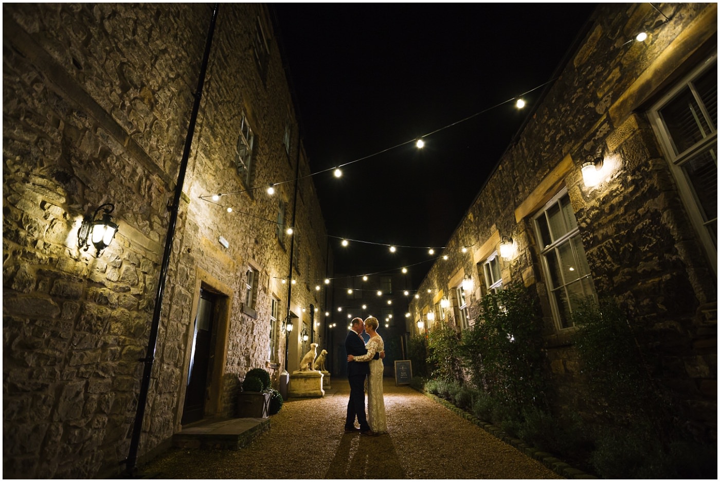 Couple stand under festoon lights at Holmes Mill Wedding