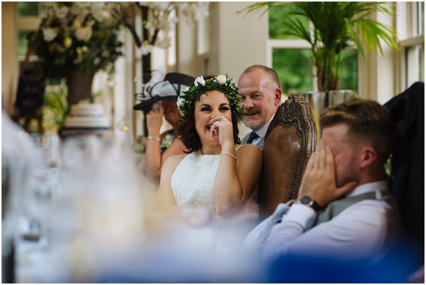 Bride laughs as groom holds head in hands during best mans speech