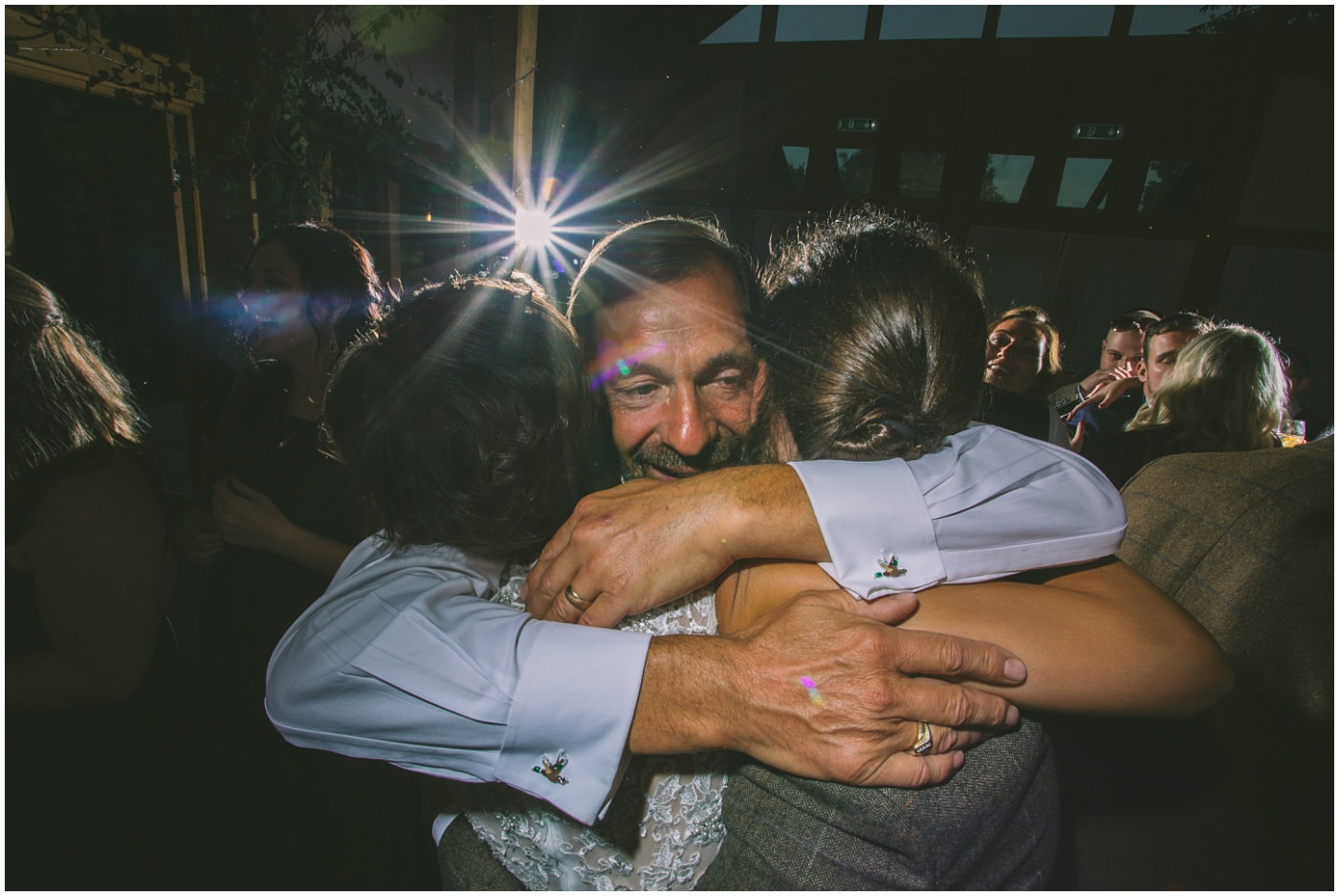 Dad hugs bride and groom on dance floor