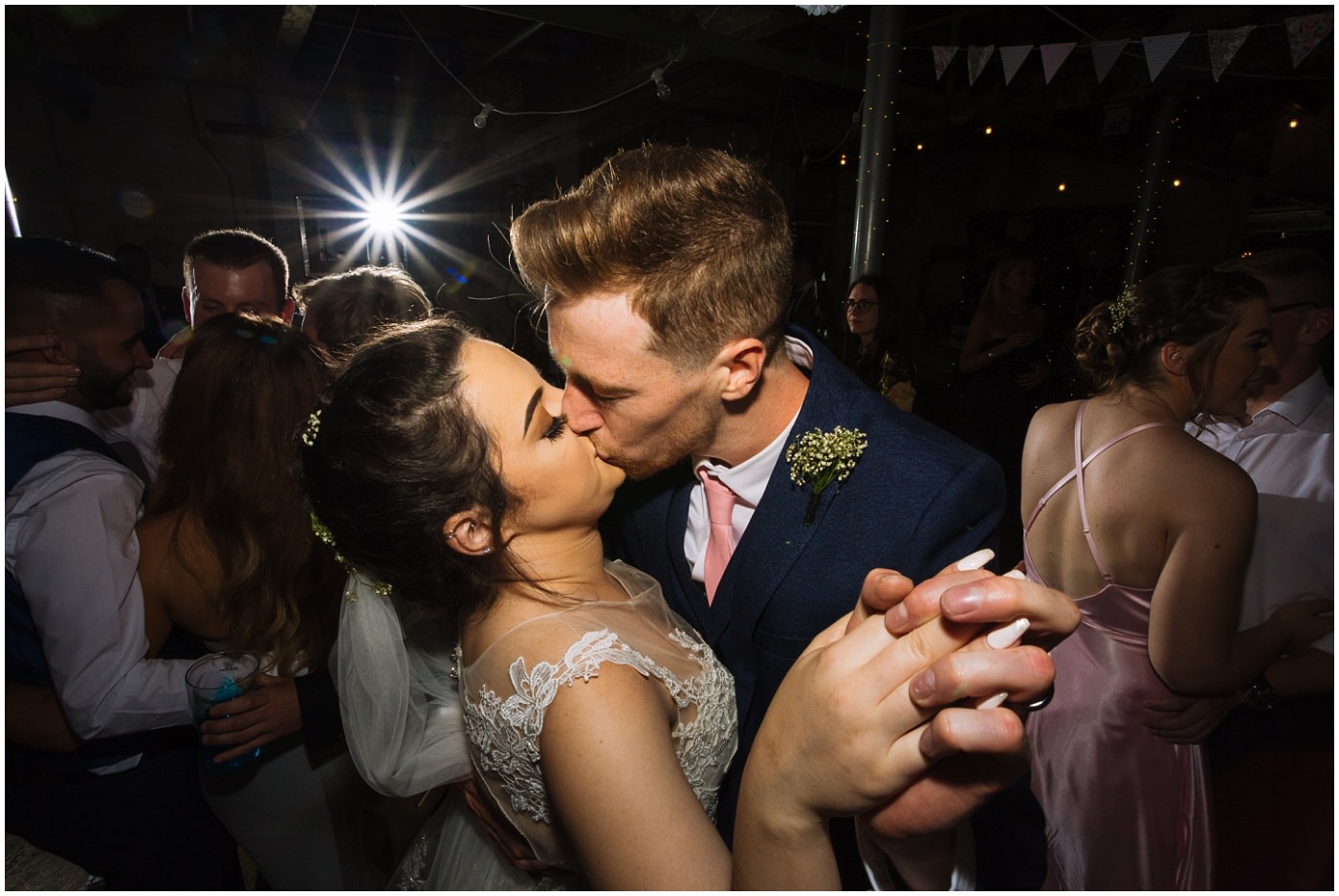 bride and groom kiss on dance floor surrounded by wedding guests