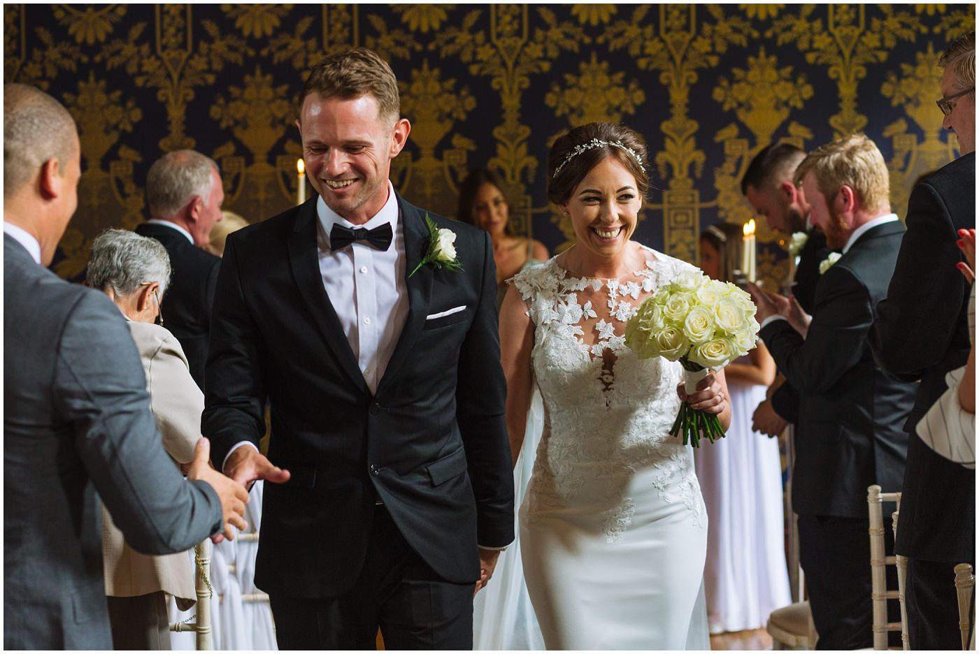 bride and groom leave ceremony room at Soughton Hall and groom shakes hands with a guest