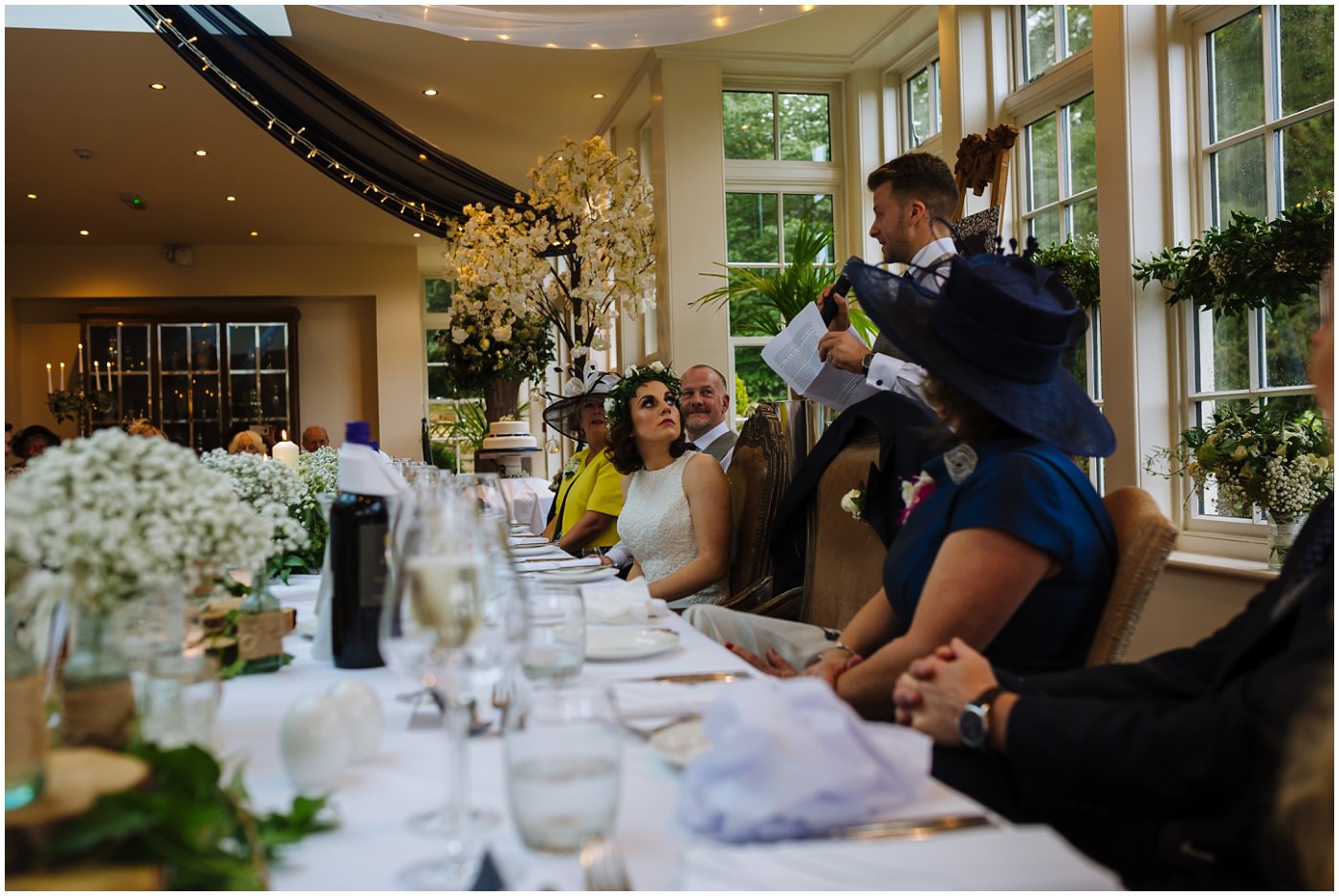 bride looks on at groom as he gives speech