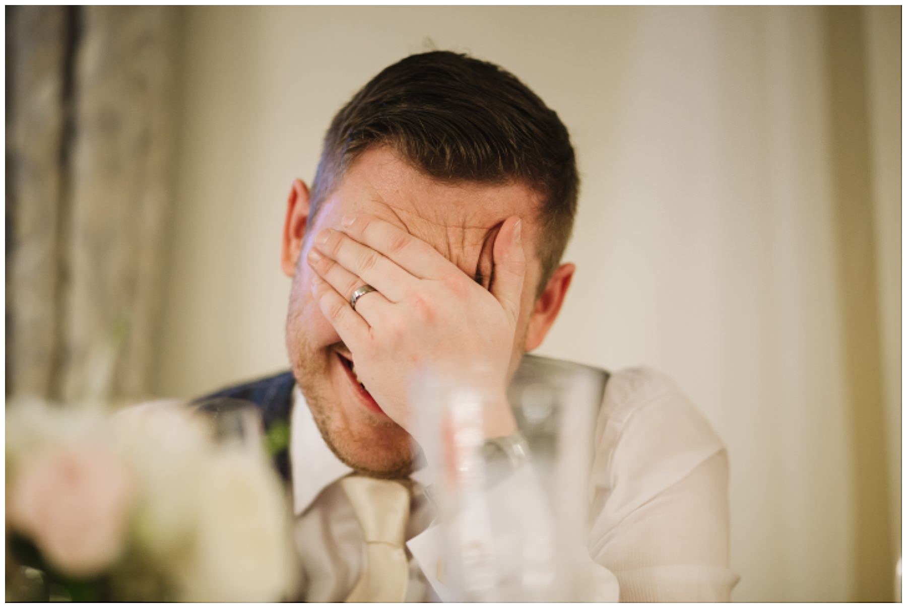 groom holds his head in his hands inn reaction to best mans speech