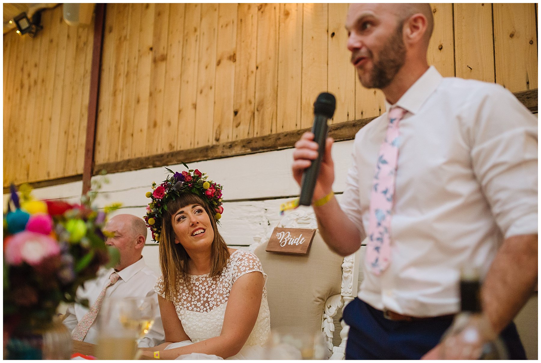 bride looks at her husband as he gives a speech at the wellbeing farm wedding