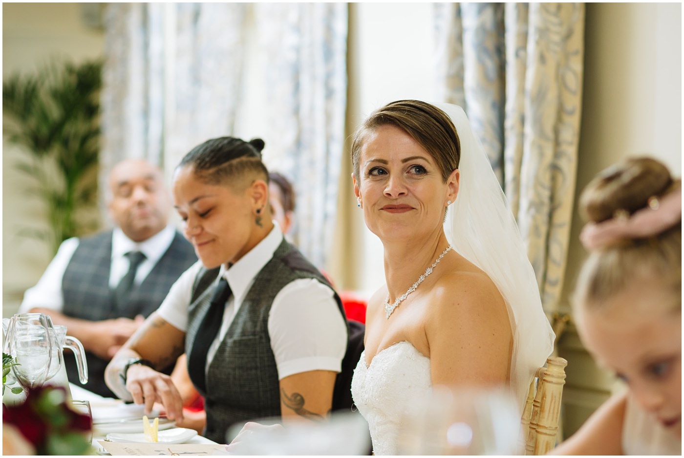 Bride looks on during wedding speeches at eaves hall