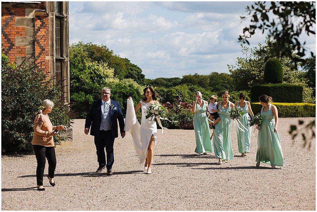 bride and bridesmaids walk to garden ceremony at arley hall