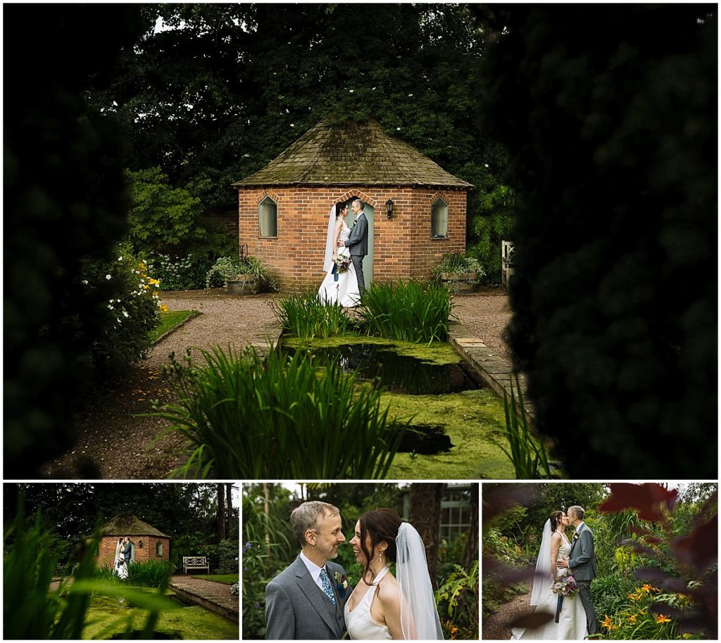 A couple embraces in a lush garden, surrounded by greenery and flowers near a charming brick structure, capturing intimate wedding moments.