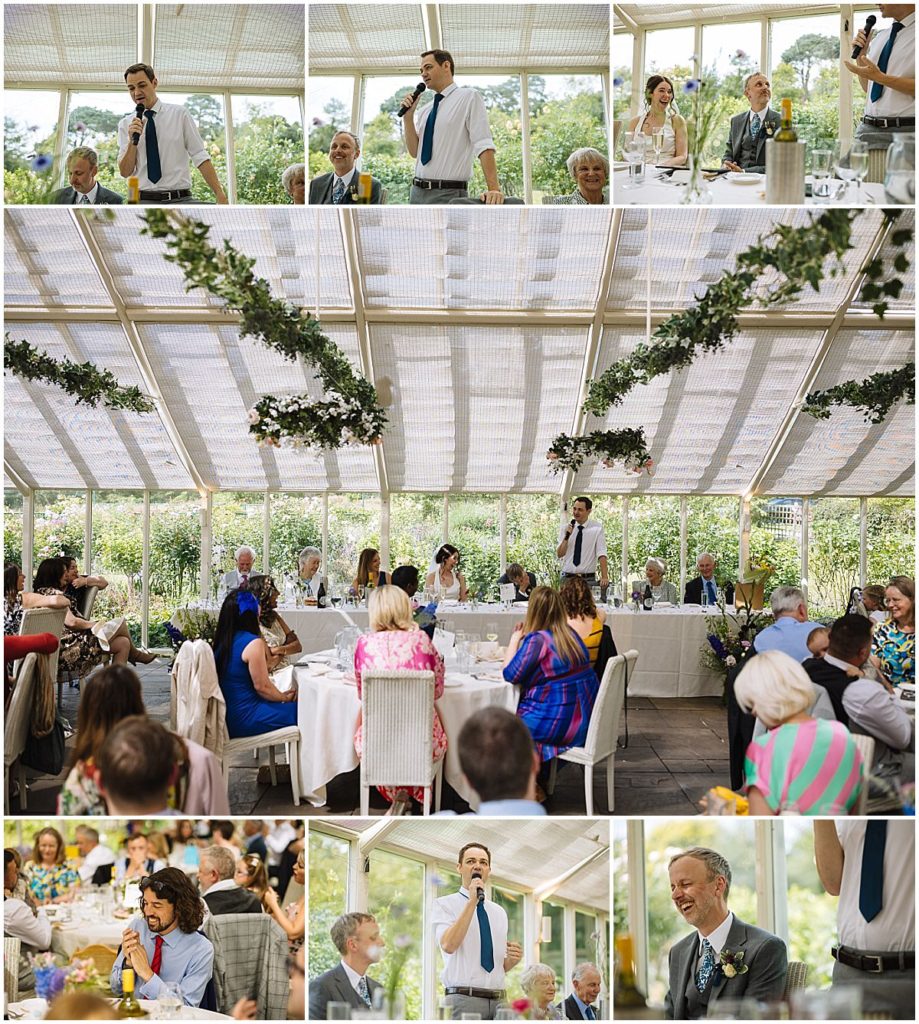 A heartfelt speech is being delivered at a wedding reception, with guests enjoying the atmosphere in a beautifully decorated glass conservatory filled with greenery.