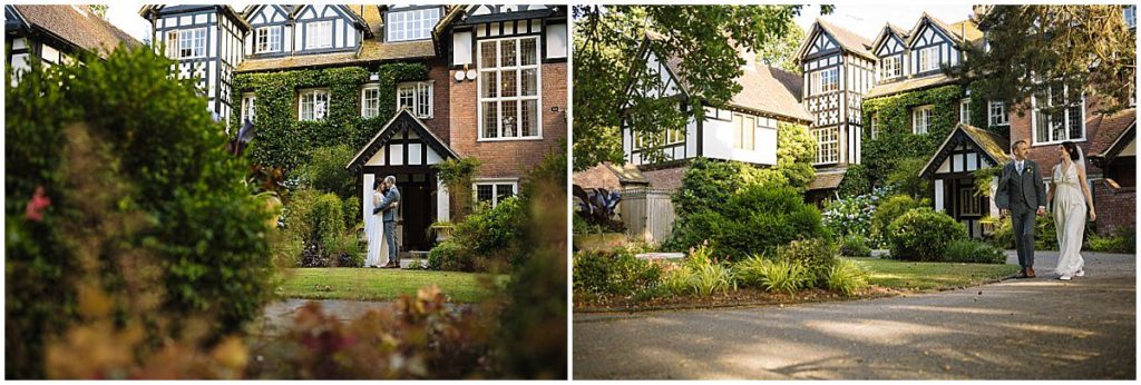 A couple shares an intimate moment in front of a beautifully landscaped manor house, surrounded by greenery and vibrant flowers.