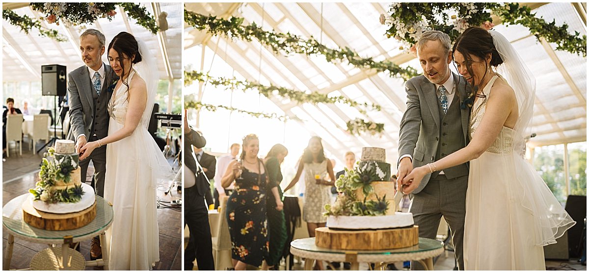 A couple joyfully cutting their wedding cake in a beautifully decorated venue with guests in the background.