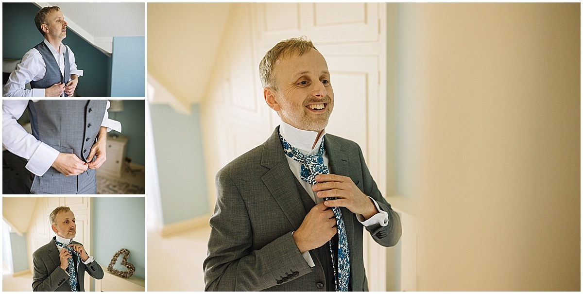 A man joyfully adjusting his tie while dressing in a stylish suit, surrounded by a light-filled room.