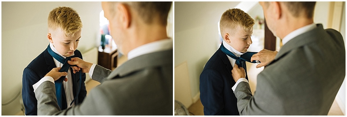 A young boy in a suit receives help adjusting his tie from the groom
