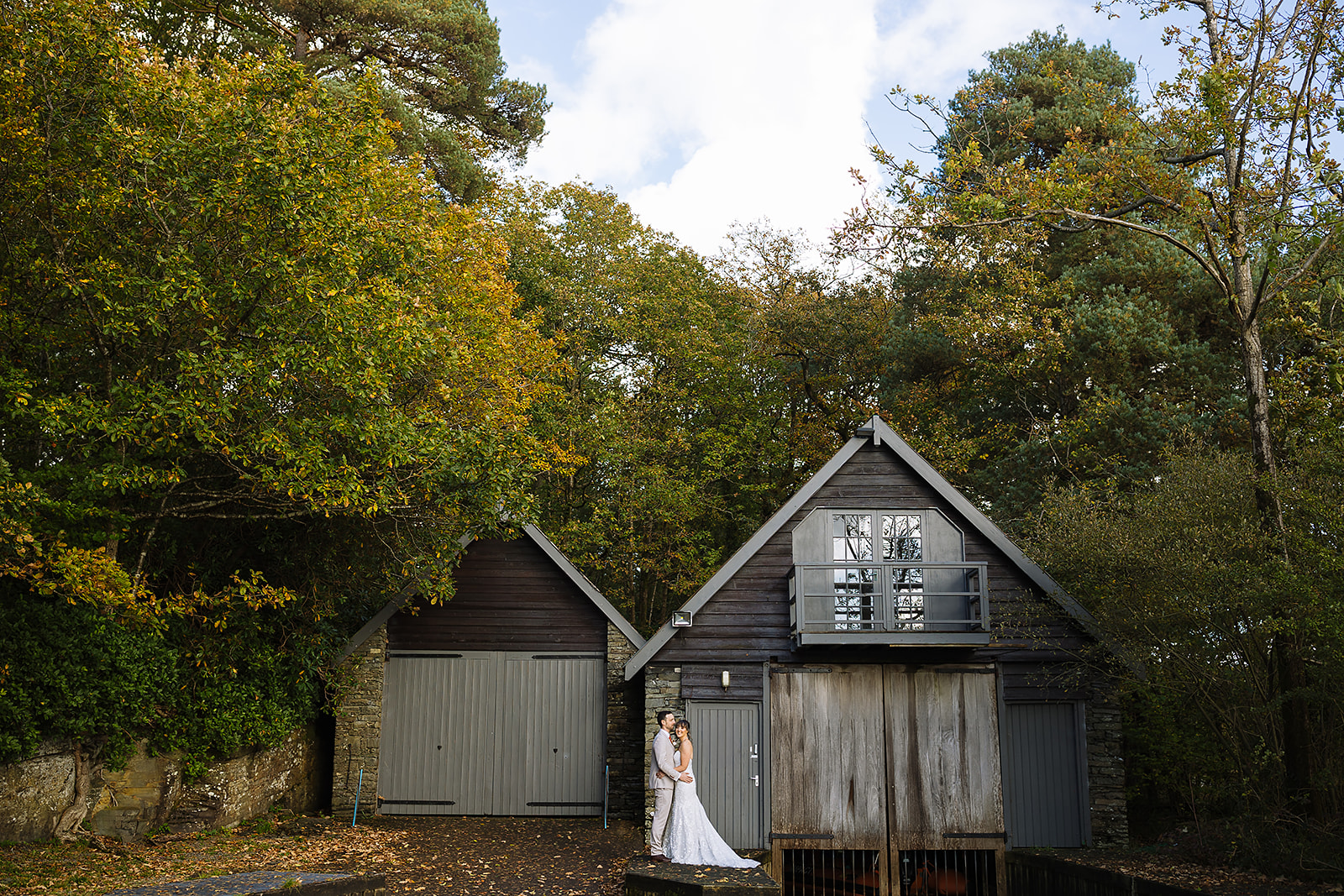 A couple embraces in front of a rustic wooden cabin surrounded by vibrant autumn foliage in the Lake District